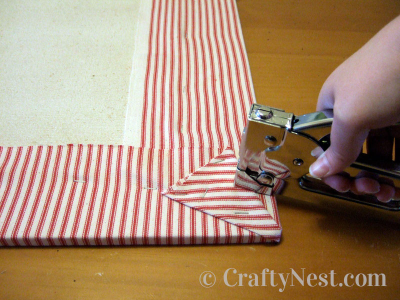 stapling-diy-bulletin-board-with-shutters-crafty-nest Stapling the fabric to the homasote board, photo