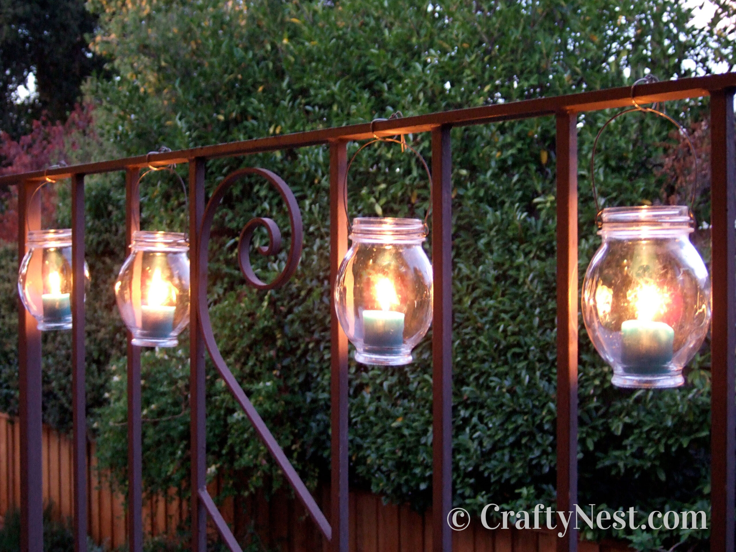 hero-diy-hanging-jar-lanterns-crafty-nest Jars with candles hanging from wire attached to a railing, photo