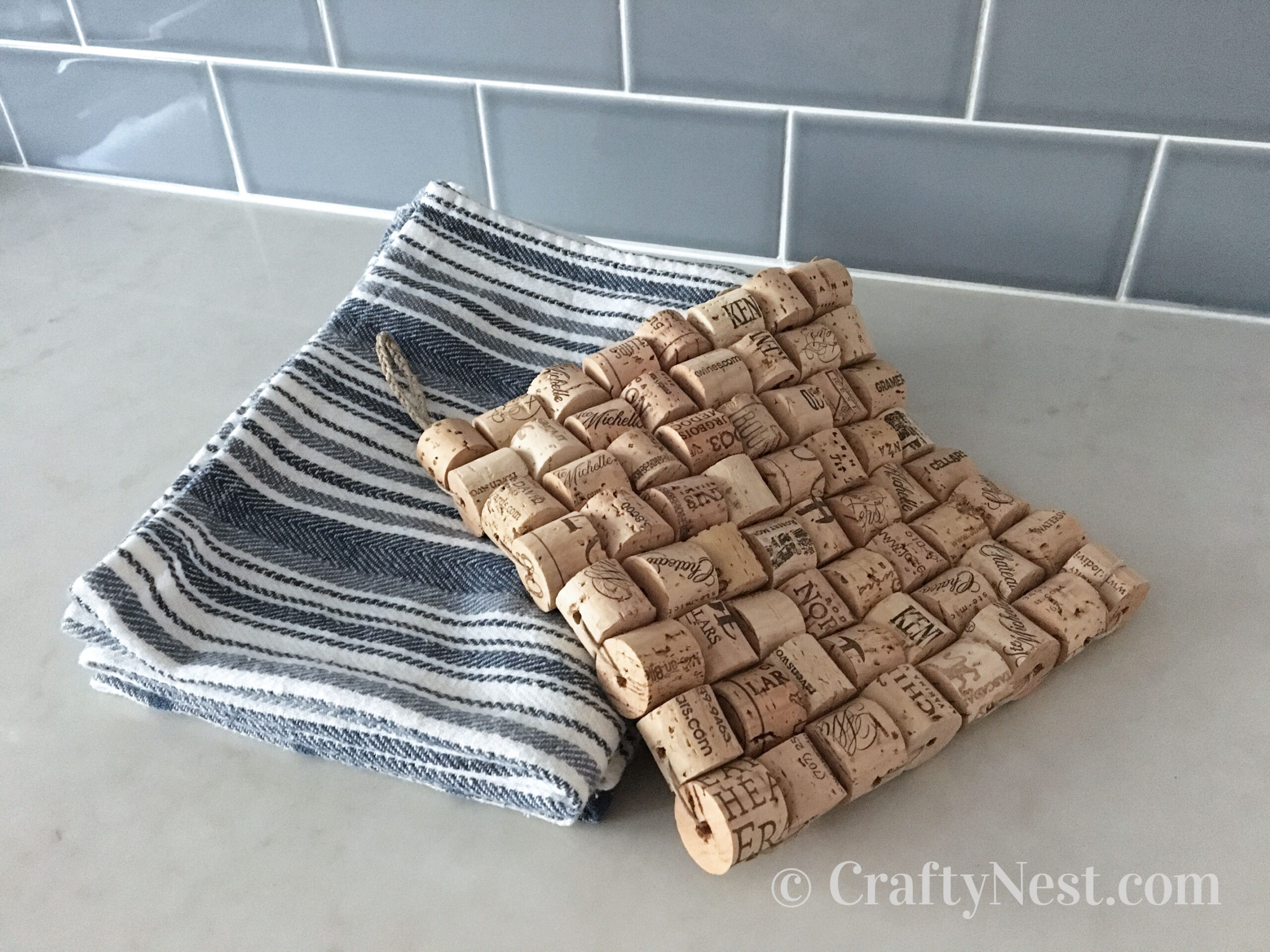 towels-woven-wine-cork-trivet-crafty-nest Wine cork trivet draped over a stack of dish towels, photo
